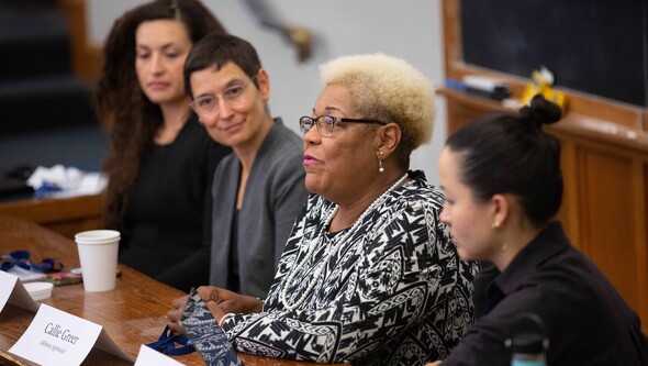 Four women sit at the front of a classroom listening to the woman in the center speaking