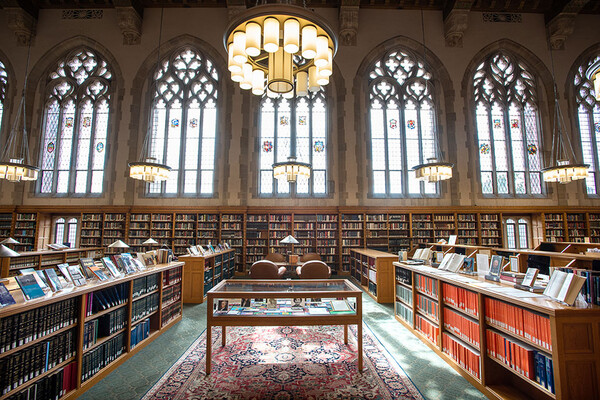 The bright interior of the Lillian Goldman Law Library with chandeliers, arched stained glass windows, and display cases.