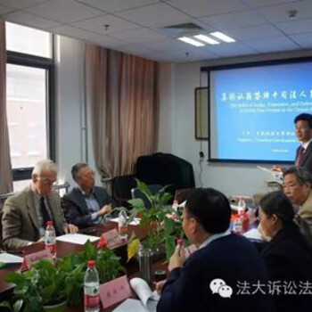 People seated at a conference room table. A video screen in the background displays Chinese characters.