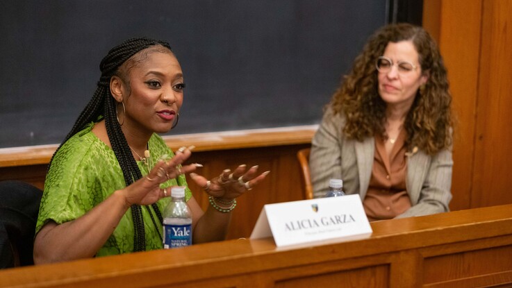 Alicia Garza seated at the front of a classroom talking while Claudia Flores looks on from the right