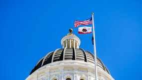 The dome of the California State Capitol against a blue sky with the U.S. and state flags waving in the breeze