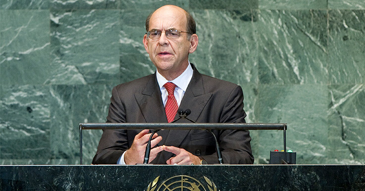 stuart beck speaks at a podium at the United Nations with a green marble wall in the background